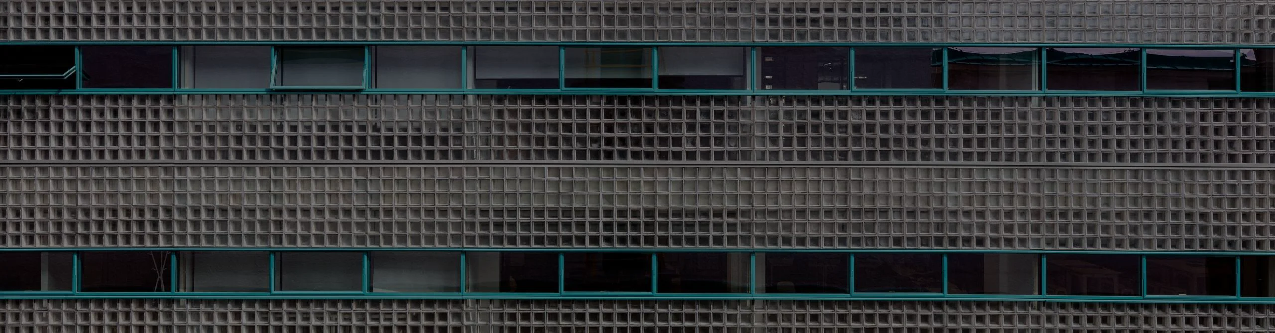 Completed building facade with repeating glass block panels and teal-framed windows.