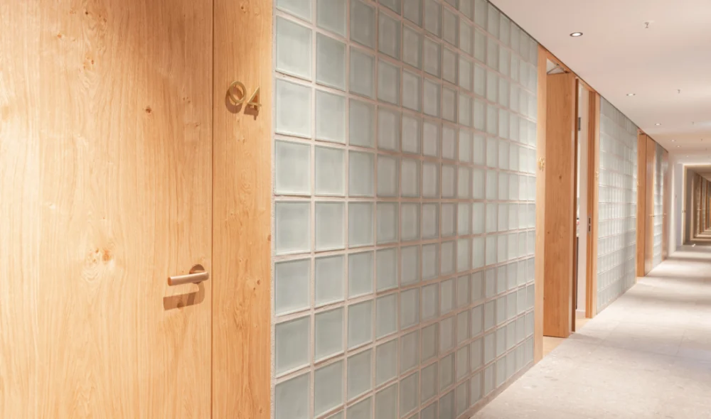 Completed hallway with a full-height translucent glass block partition and warm timber doors.