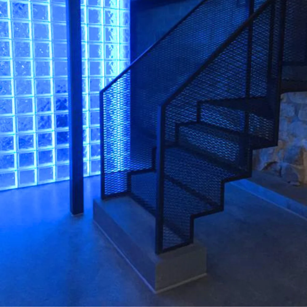 Completed stairwell with a blue-lit glass block wall and dark metal stair railing.