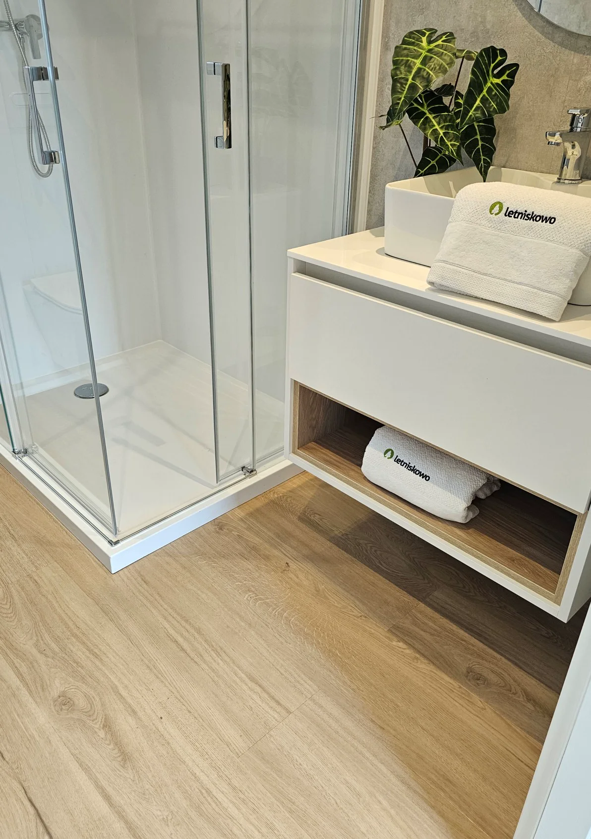 Wood-effect flooring installed in a bright bathroom beside a shower and vanity.